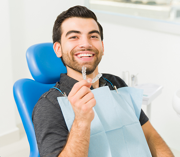 Man in dental chair holding mirror, smiling at dentist's office during checkup.