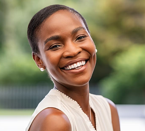 Smiling woman in white shirt outdoors at Woodland Dental practice setting.