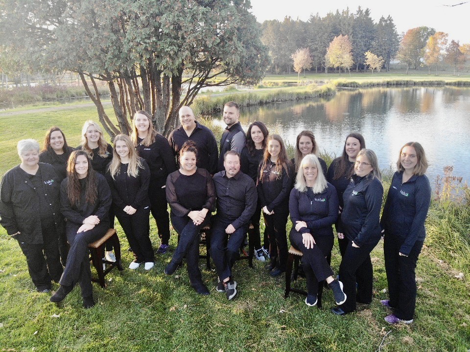 Woodland Dental team posing together outdoors by river with trees in background.